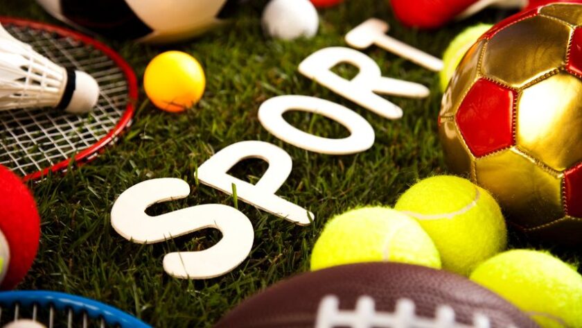 Sport w kulturze – na zdjęciu napis sport z białych liter na trawie, a wokół niego różne piłki i akcesoria sportowe.
