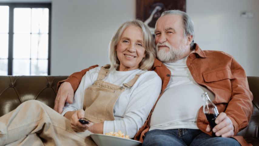 Starsze małżeństwo ogląda filmy dla seniorów, siedząc na sofie.