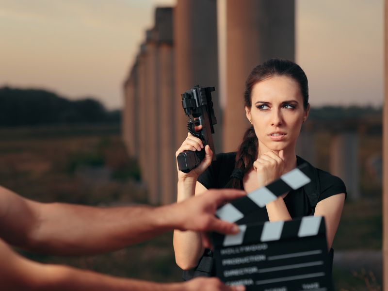 CO cechuje dobre filmy akcji? Na zdjęciu aktorka z pistoletem przed sceną.